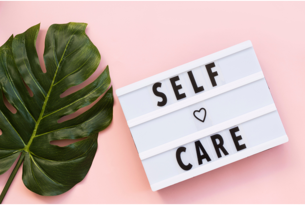 Bord met tekst "self care" met roze achtergrond en groot blad aan de linkerkant